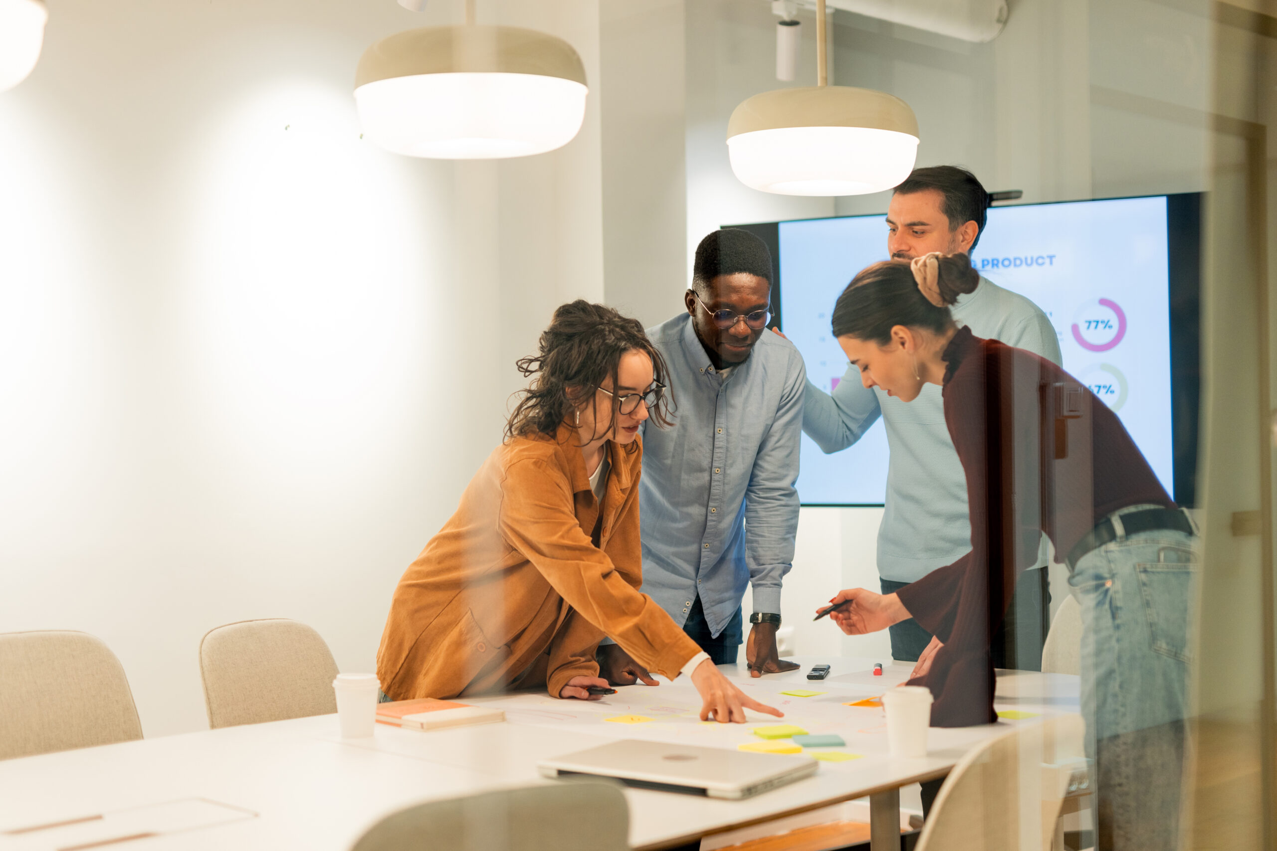 Team gathered around a conference table with sticky notes and a data screen behind them.
