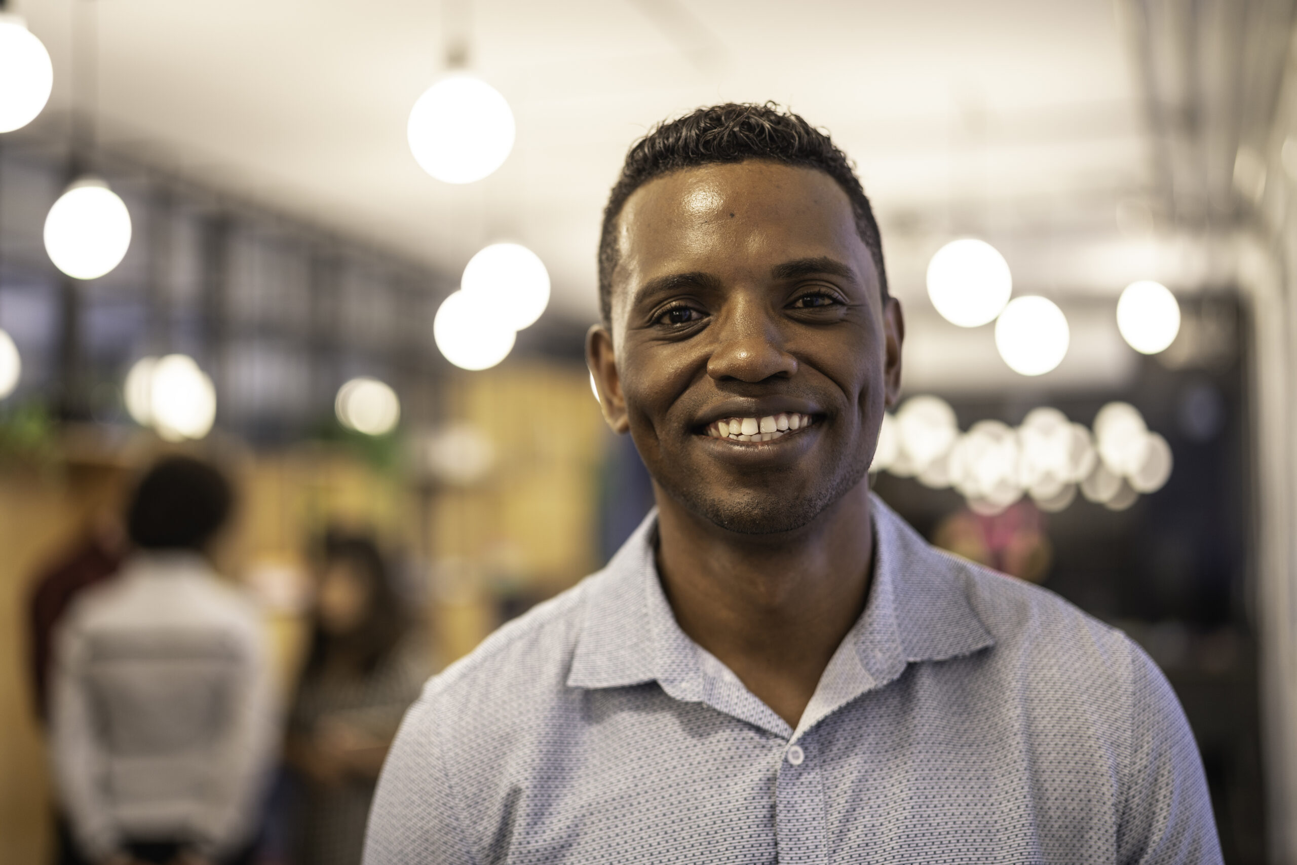 Founder smiling in an open workspace with colleagues working in the background.