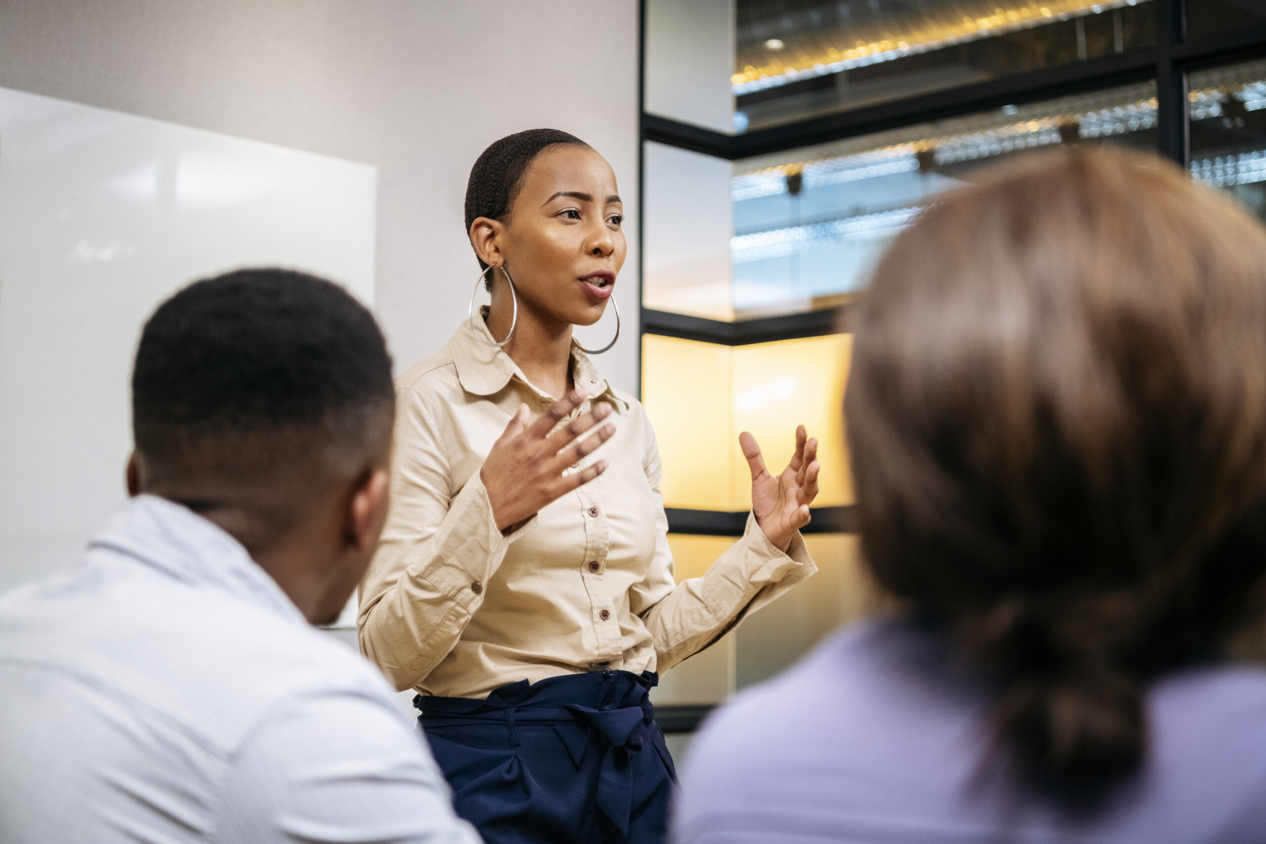 Leader speaking to colleagues around a table in a modern office, hands open mid-explanation.